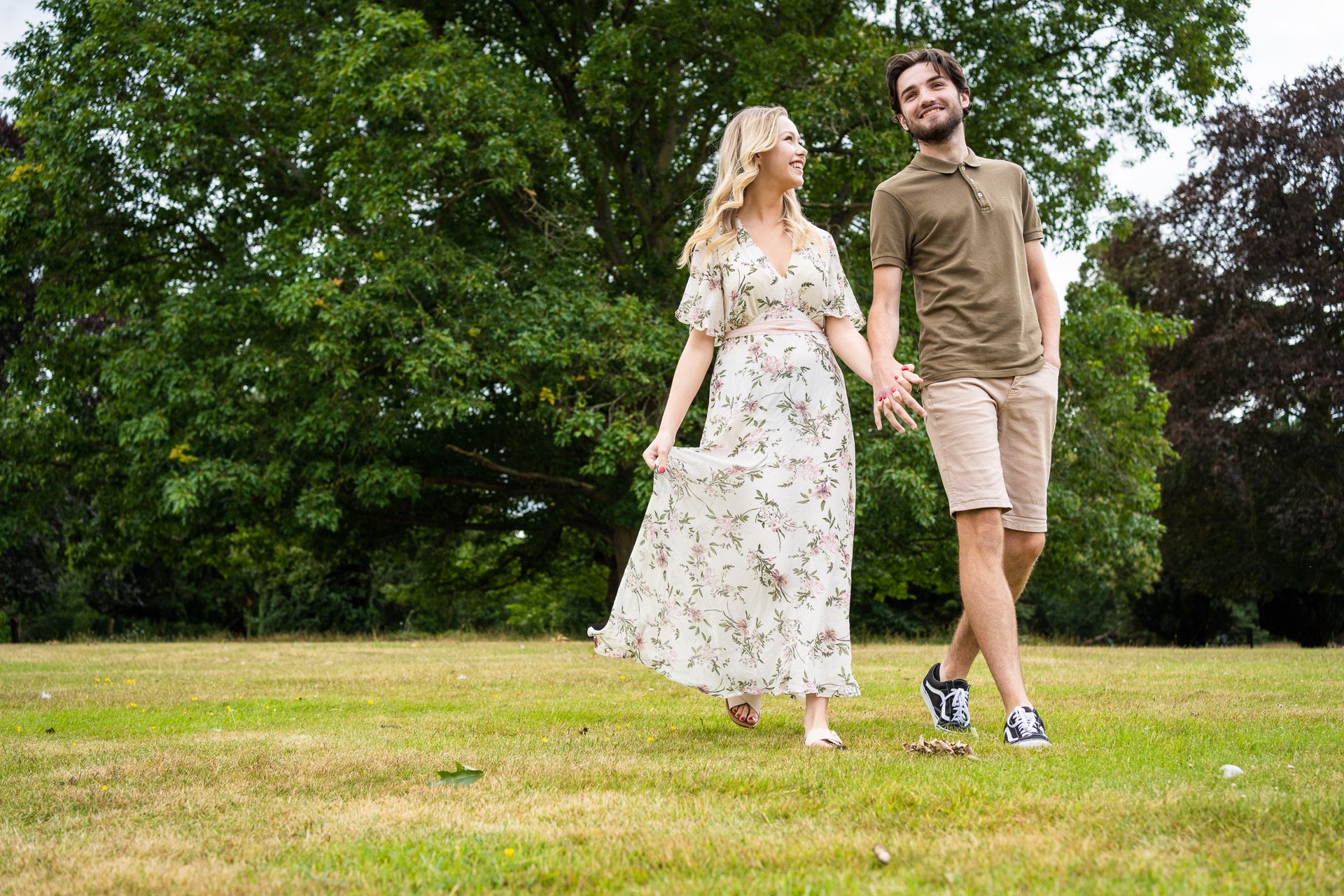 Wedding Photography Packages - Couple strolling in a park with trees in the background, wearing summer clothes