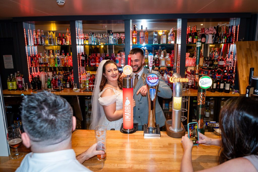 Bride and Groom posing behind the bar at the Fennes Essex. Taken by Tim Payne Photography, a Hertfordshire wedding photographer