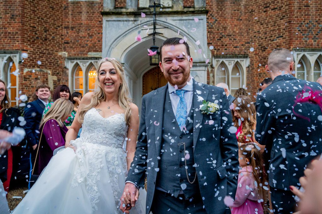Bride and Groom walking through confetti at Hertford Castle. Taken by Tim Payne a Hertford wedding photographer.