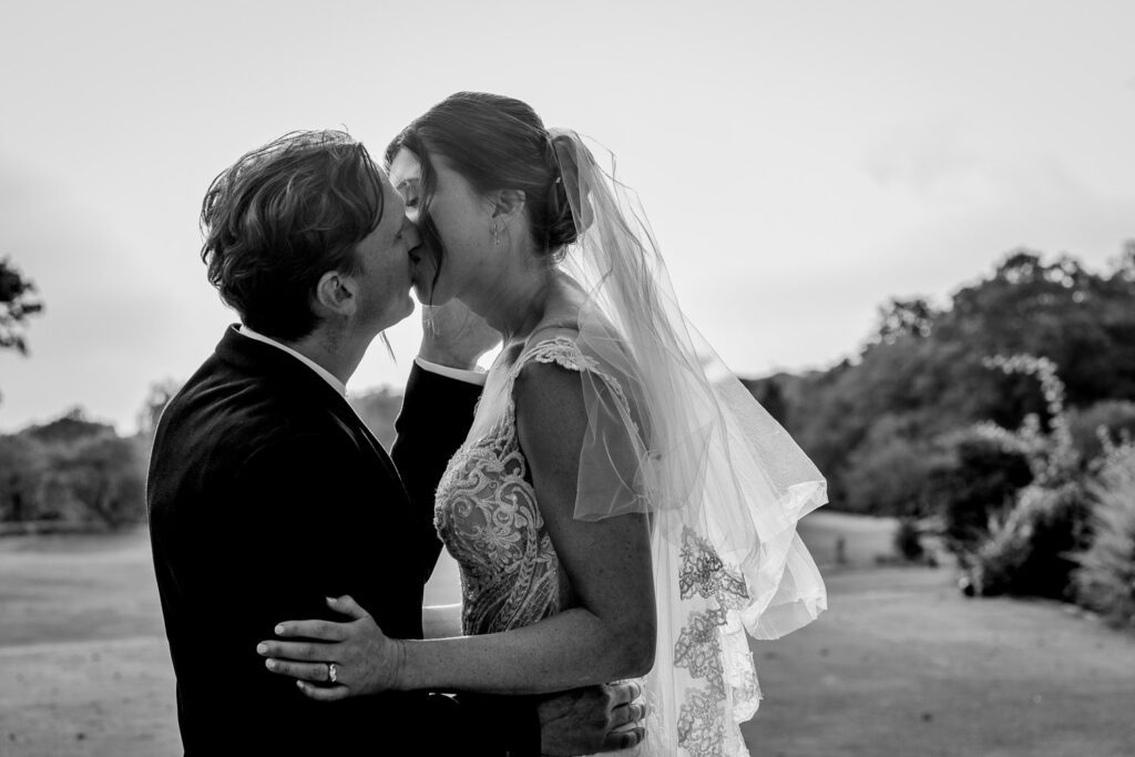 Black and white image of a Bride and Groom sharing a kiss in the grounds of Brickendon Grange . Taken by Tim Payne Photography