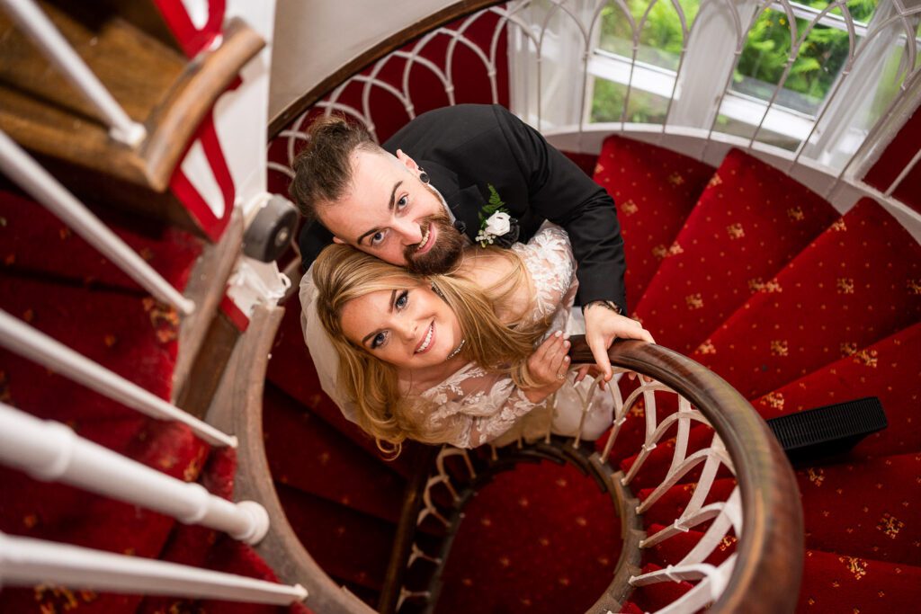 A newly married couple standing on the spiral staircase in Hertford Castle . Taken by Tim Payne Photography