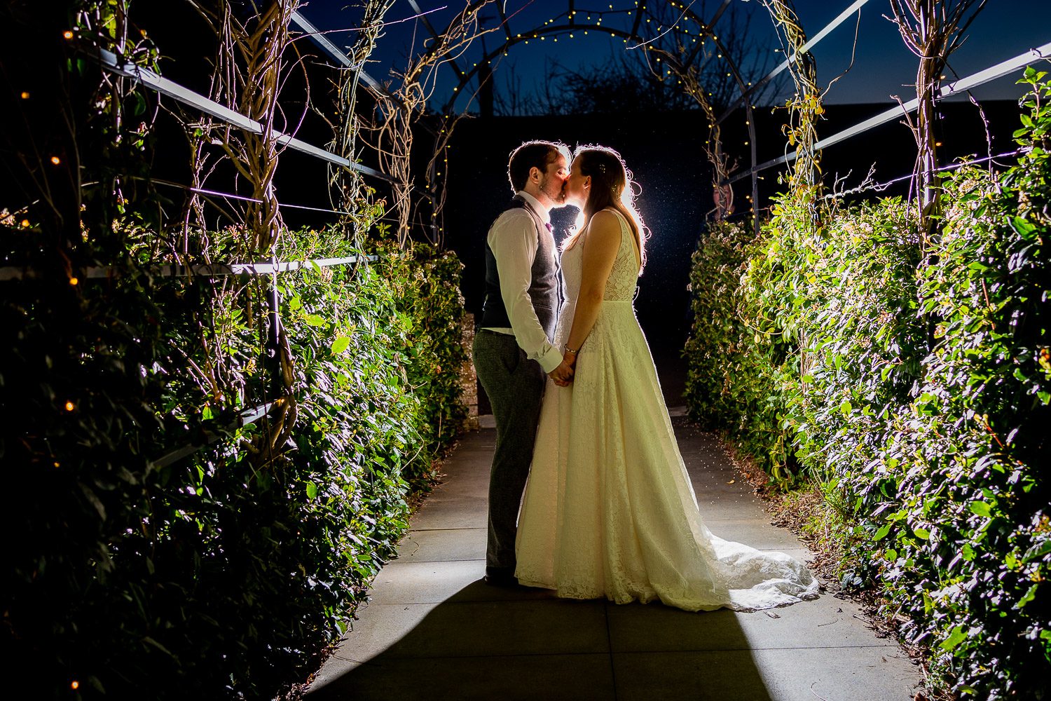  a bridal couple kiss in the moonlight under an arbour in the gardens