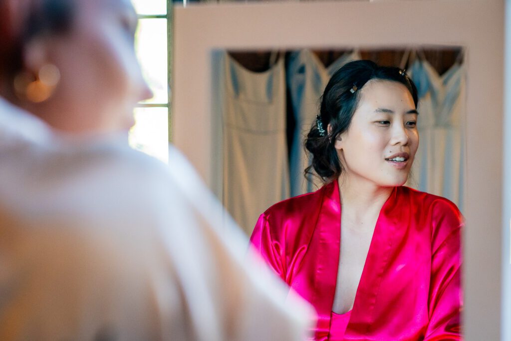 Cindy, a beautiful bride getting ready at Fanhams Hall in Ware. A photograph taken of her reflection in a wall mirror. Tim Payne Photography, a Hertfordshire wedding photographer