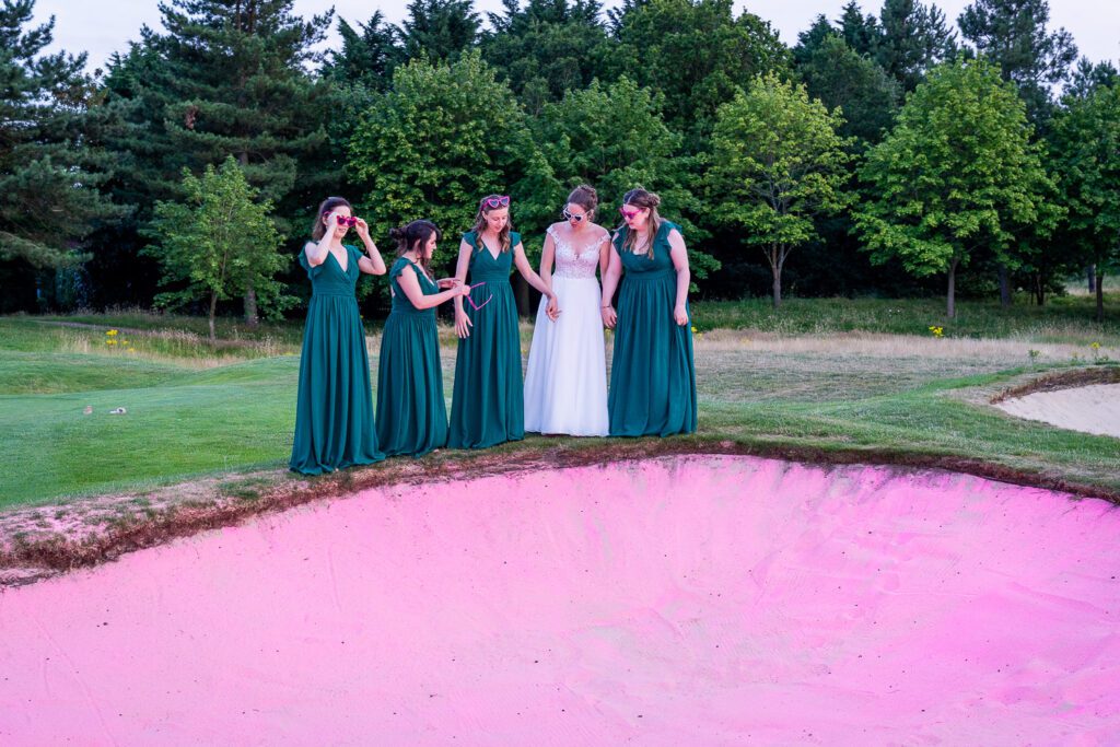 Bride and her bridesmaids standing on top of a sand bunker with pink sand, at Essendon country club. Tim Payne photography, a Hertfordshire based wedding photographer