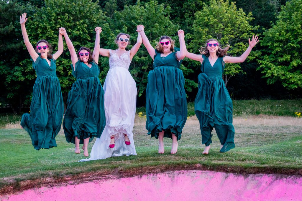 Bride and her bridesmaids jumping up at the edge of sandtrap on a golf course. Tim Payne Photography. Beautiful wedding photography.