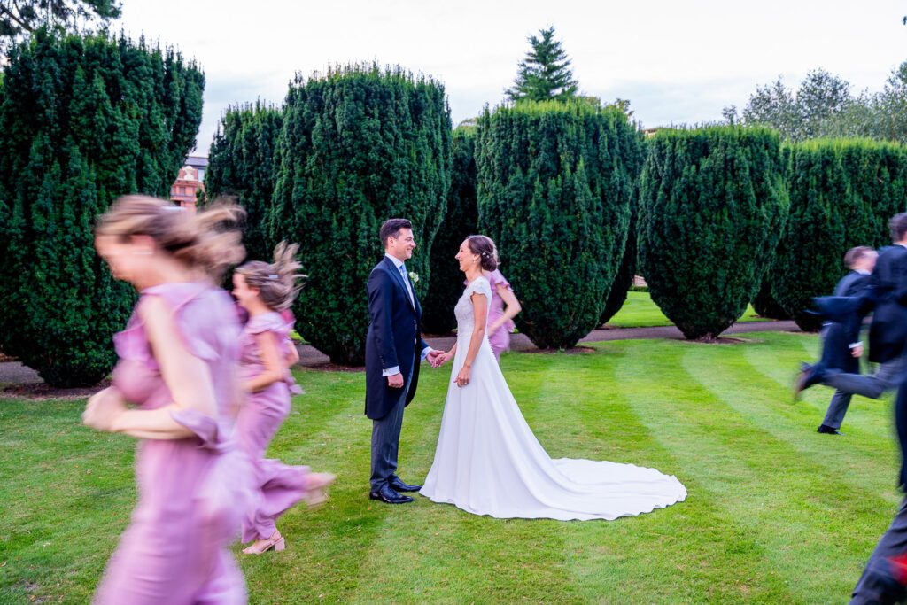 Fun photograph of the brides maids and groomsmen running around the bride and groom at the Grove Hotel, Watford. Tim Payne Photography, a Hertfordshire wedding photographer.