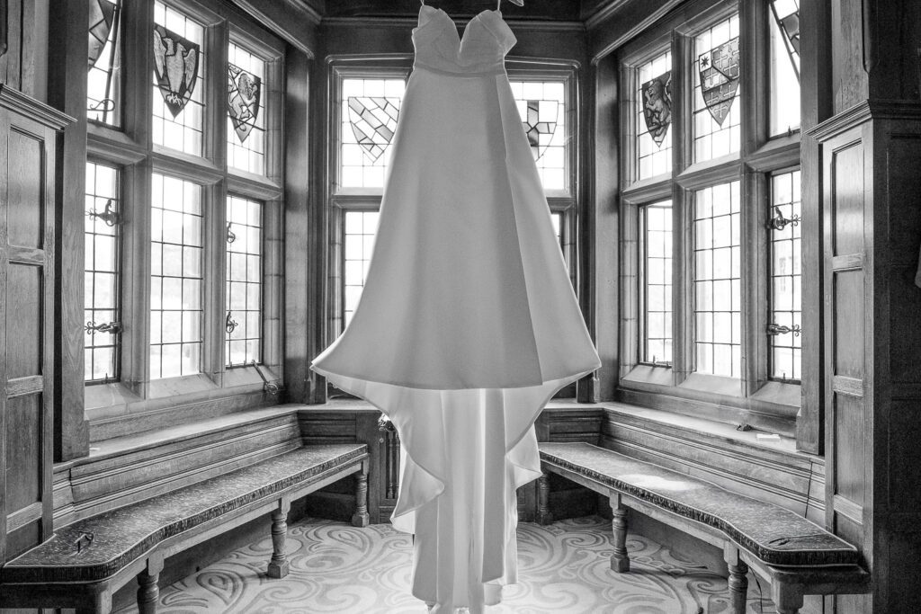 Wedding dress hanging in a bay window at Fanhams Hall, Ware (black and white image) . Taken by Tim Payne Photography, a Hertfordshire wedding photographer