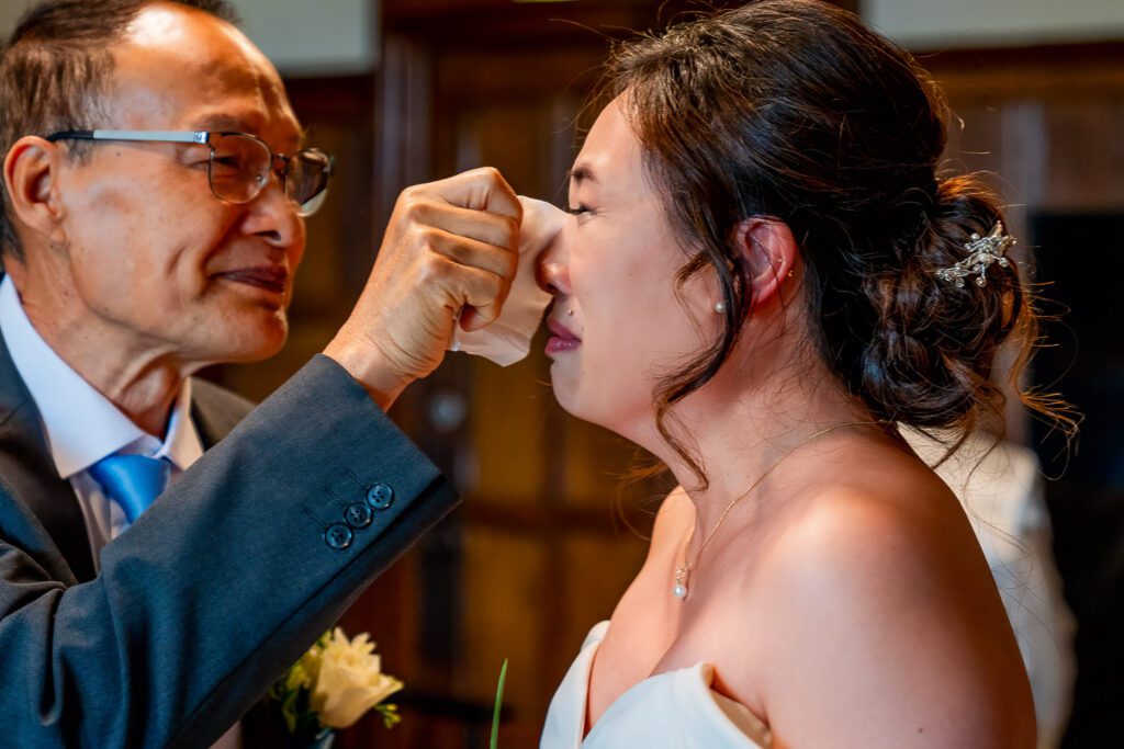 Bride having her tears wiped away by her father before she gets married at Fanhams Hall, Ware. Tim Payne Photography, a Hertfordshire wedding photographer.