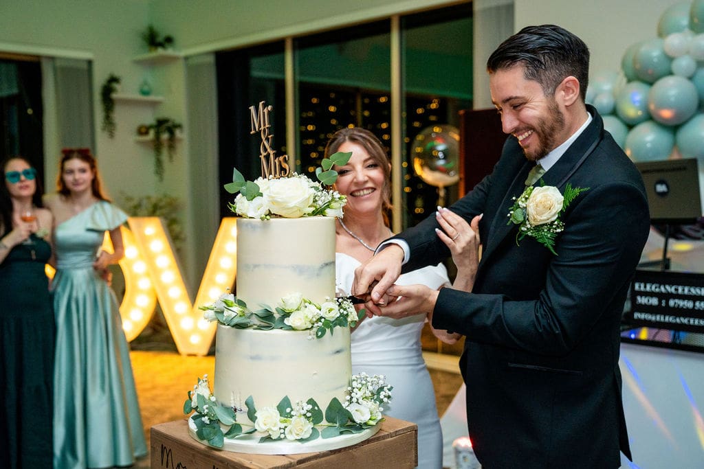 Bride and Groom cutting their 2 tier, white wedding cake with pale green and white floral deoctations