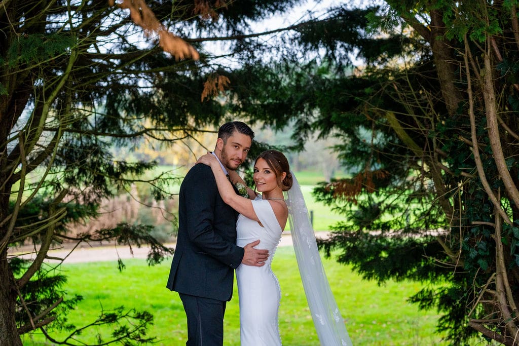 Bride and groom embracing, looking at camera framed by trees at Brickendon Grange wedding venue
