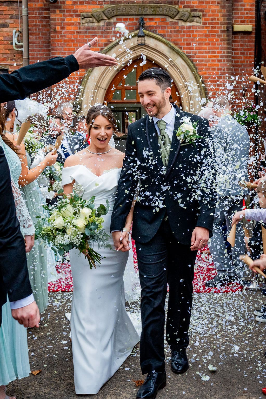 Outside Brickendon Grange wedding venue a bride and groom walk past guests showering them in confetti