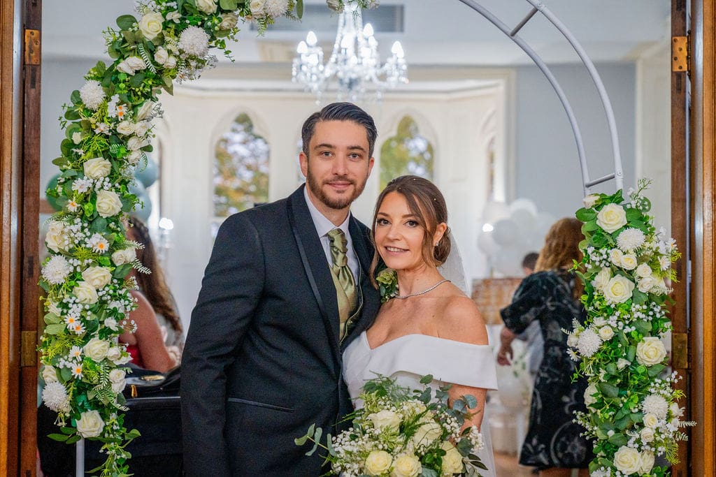 Brickendon Grange wedding venue a bride and groom, framed by a white and green floral arch in the Oak room