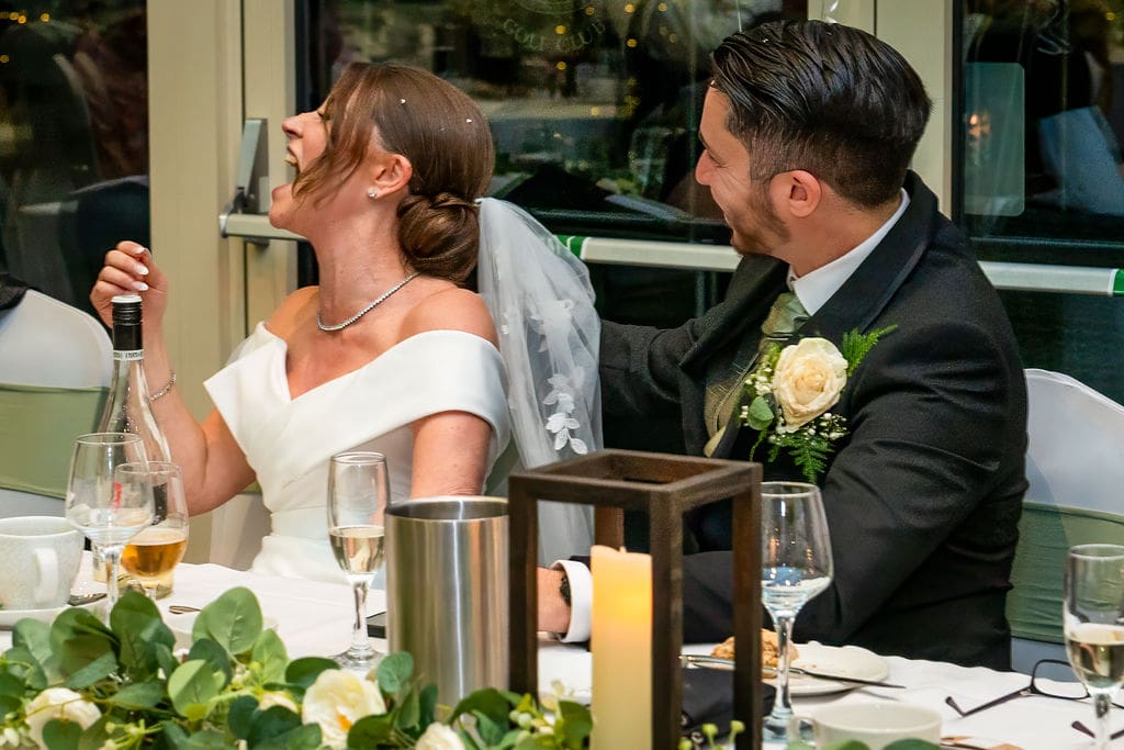 Close up of bride and groom on the top table looking to wards someone and laughing - at Brickendon Grange Wedding venue