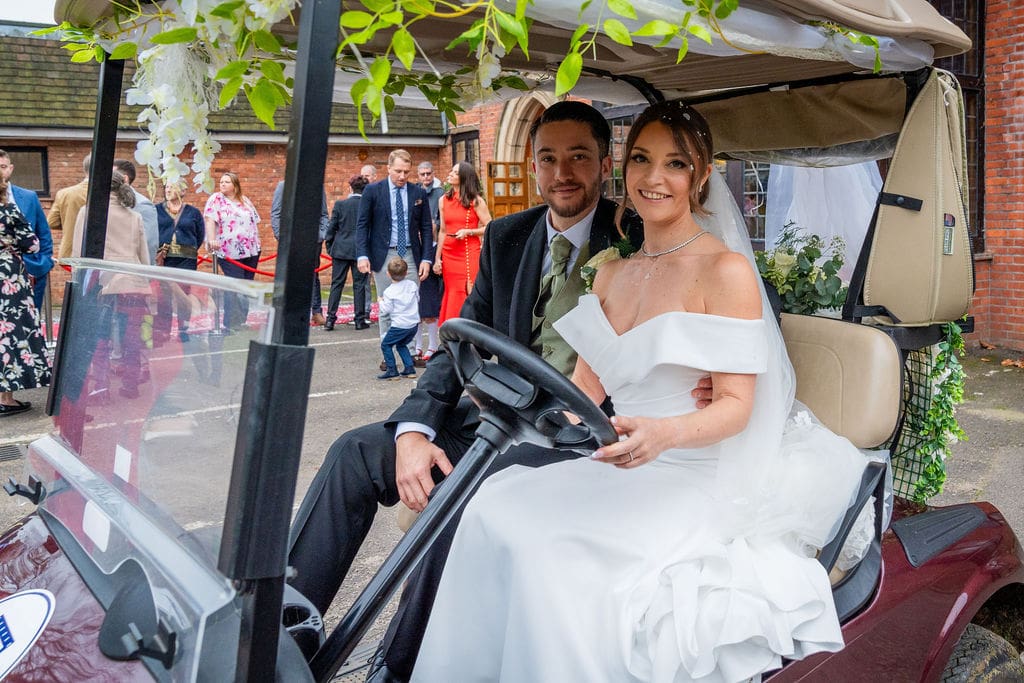 A bride and groom on a red, decorated golf cart at Brickendon Grange wedding venue
