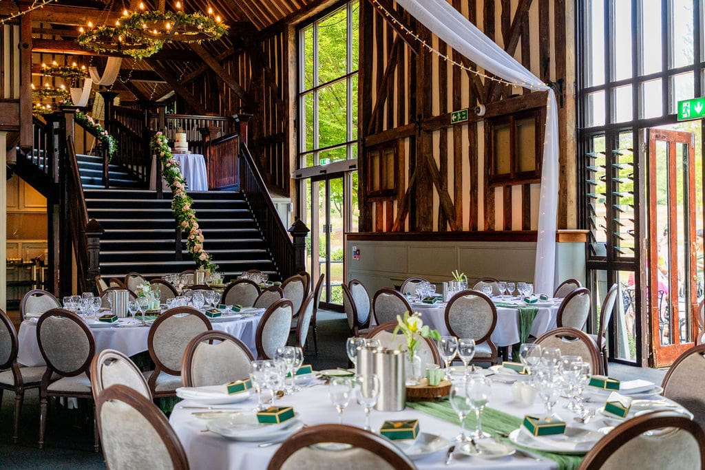 Essendon Country Club wedding venue showing large oak framed windows, beamed walls of the barn, round wedding tables and a staircase leading to the mezzanine