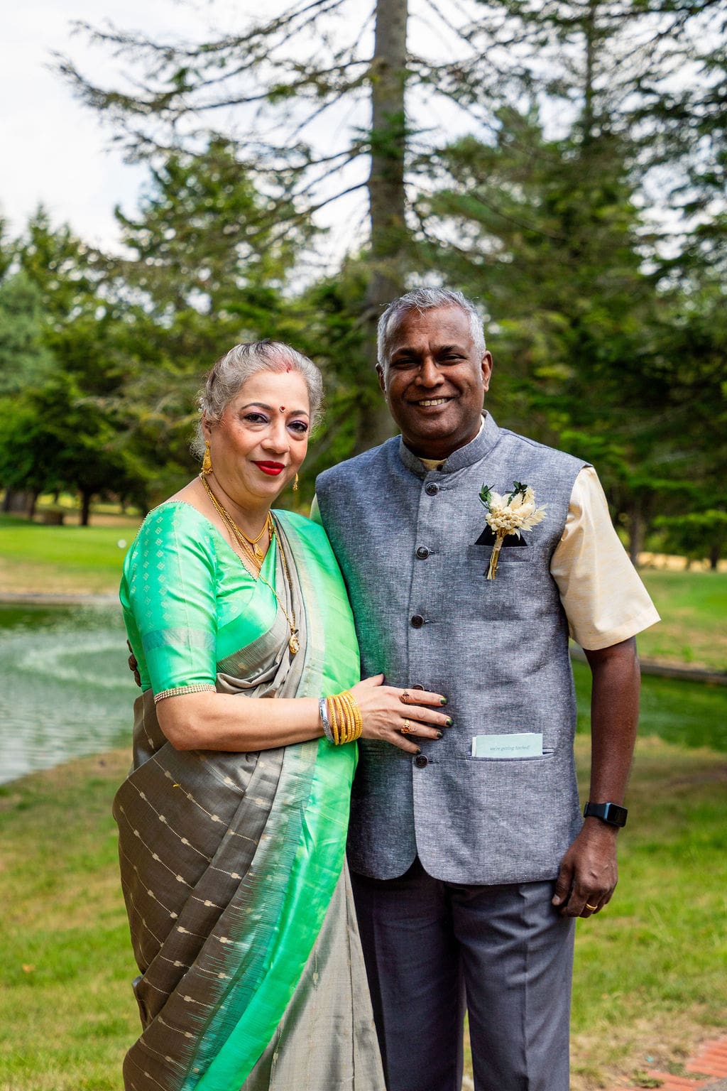 An older Indian couple in the grounds of Essendon Country Club wedding venue. The lady is wearing a beautiful green sari, the gentleman is wearing a grey sleeveless jacket with a nerhu collar.