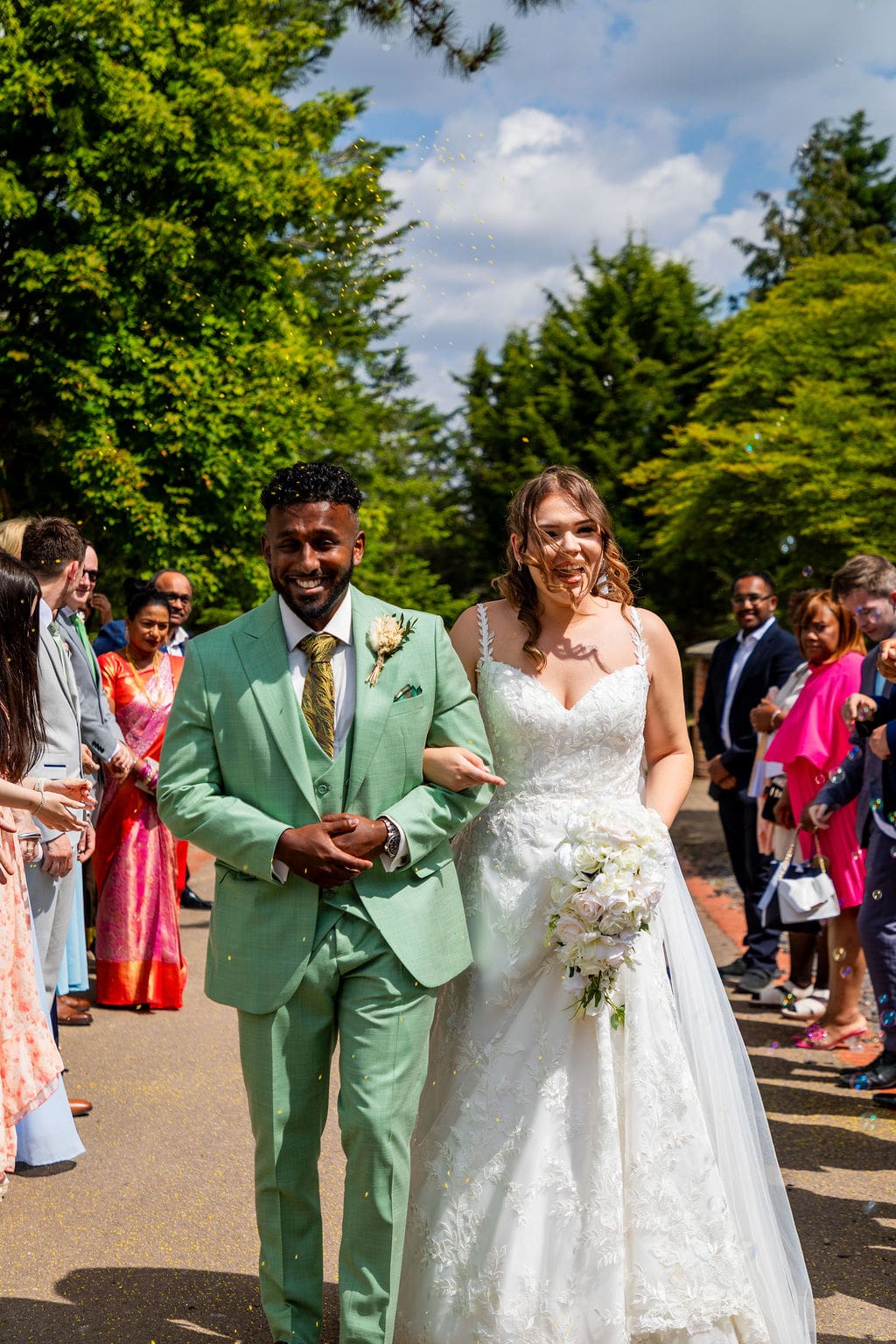 Essendon Country Club wedding venue, outside a traditional bride and her groom in a green suit walk down a path lined by guests, some of whom are dressed in colourful saris 