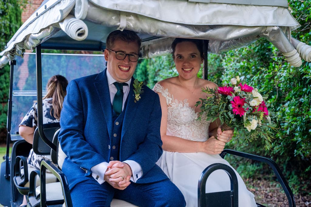 Essendon Country Club wedding venue where a traditional bride and a groom in a 3-piece blue suit sit on the back of a golf buggy laughing