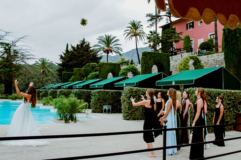 35mm film wedding photography of a bride throwing her bouquet to the female guests by the side of a pool